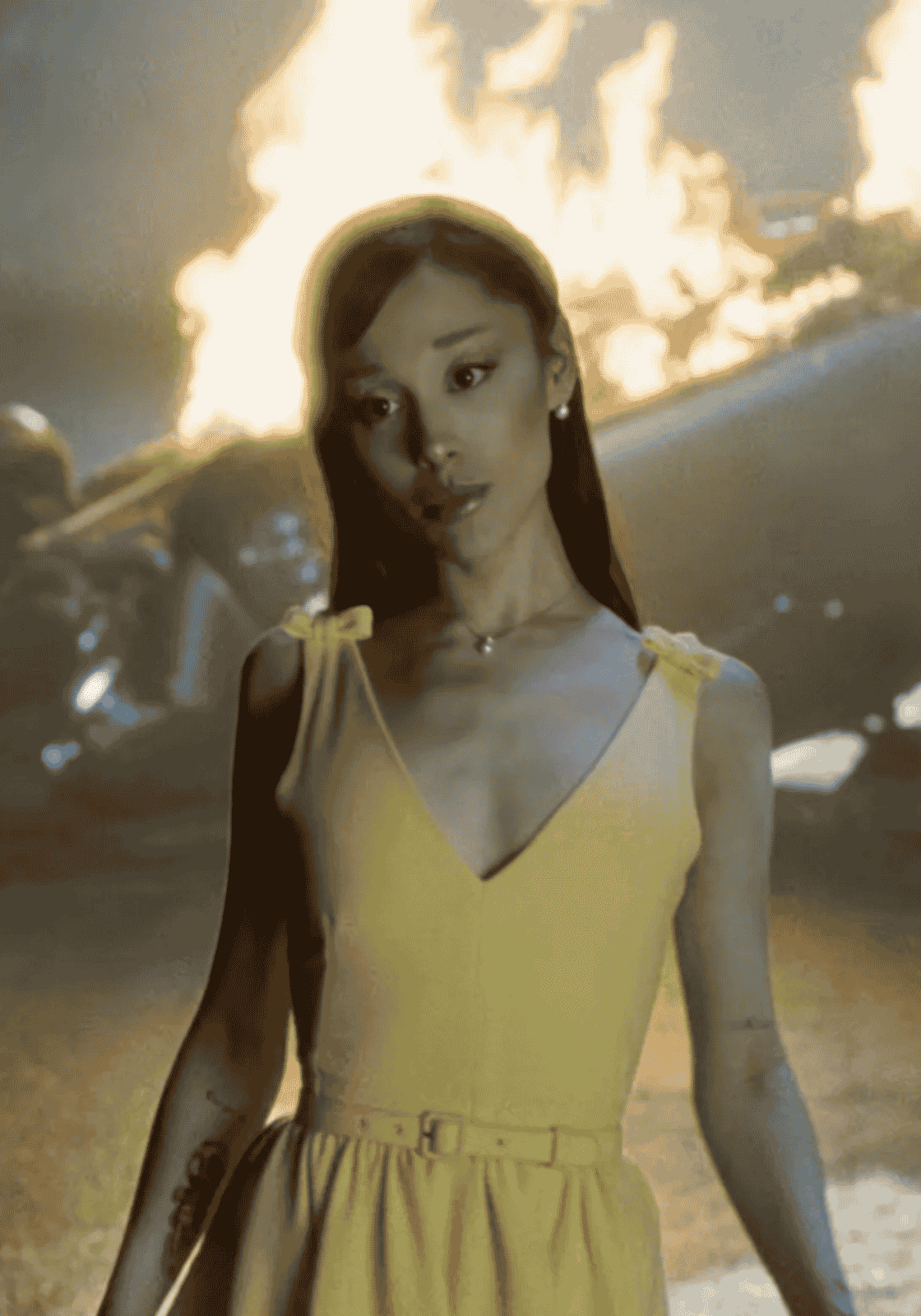 Ariana Grande sárga ruhában, lángoló autó előtt a videóklipben