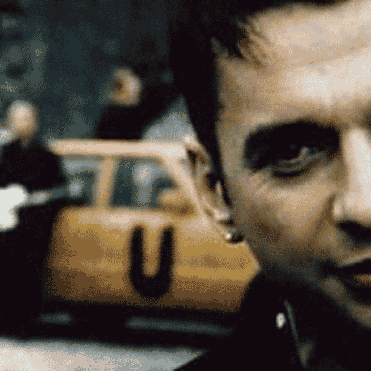 Dave Gahan közelképe a Useless klipjéből, mögötte az okkersárga autóval