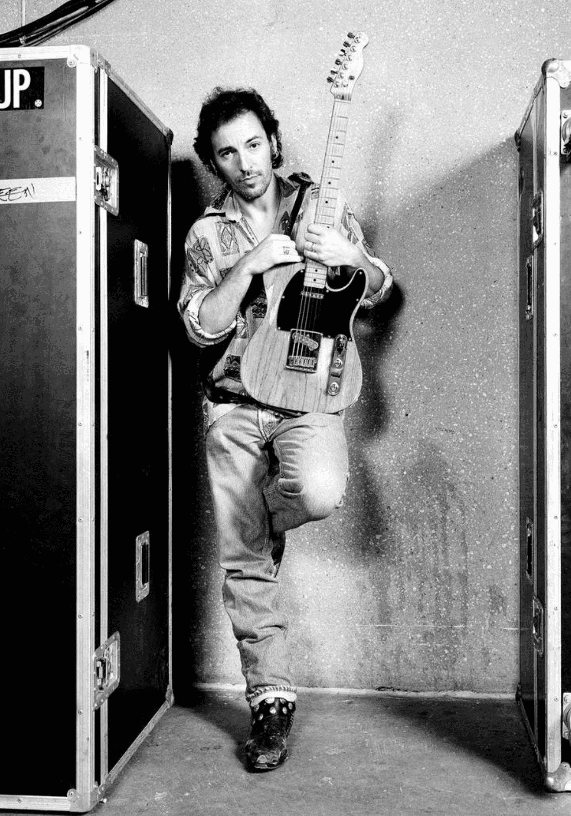 Bruce Springsteen fekete-fehér portréja gitárral, két hangszertok között