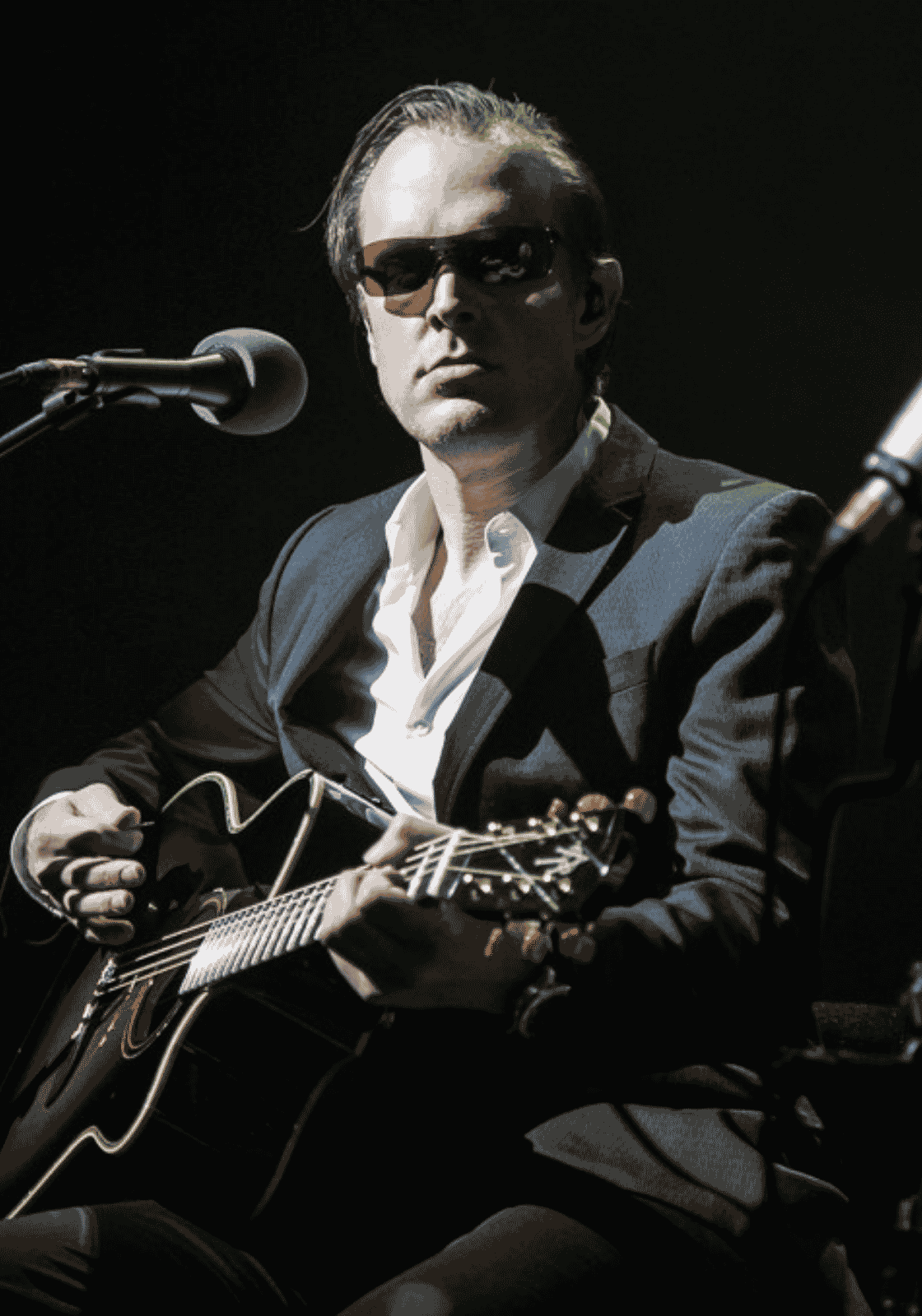 Joe Bonamassa fekete-fehér koncertképen, gitárral és mikrofon mellett