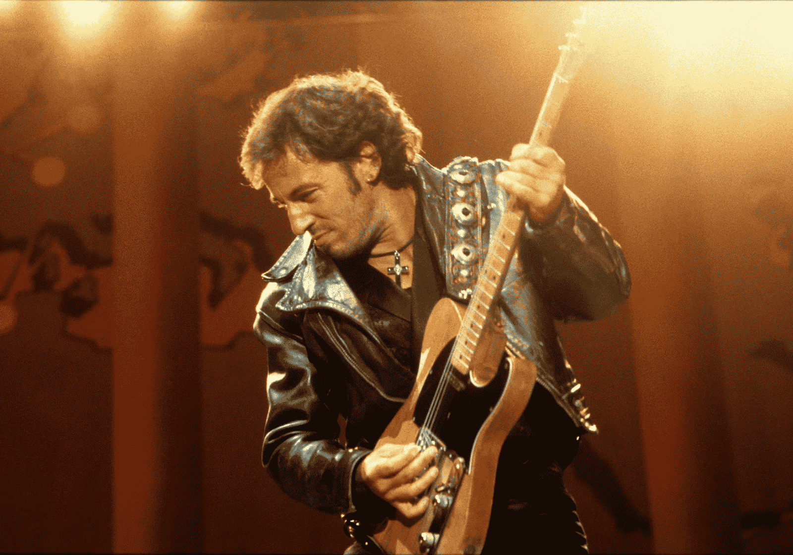 Bruce Springsteen gitározik koncert közben, aranyszínű színpadi fényben