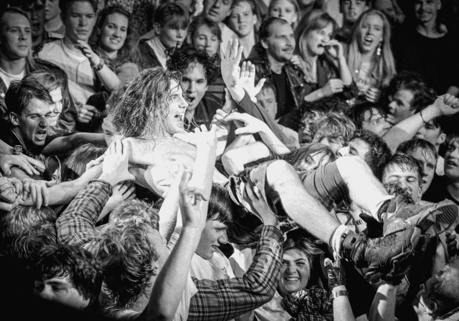 Koncertközönség fölött crowdsurfölő zenész fekete-fehér felvételen